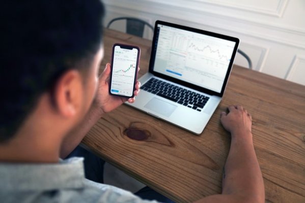 Someone checking their stocks on their phone and computer